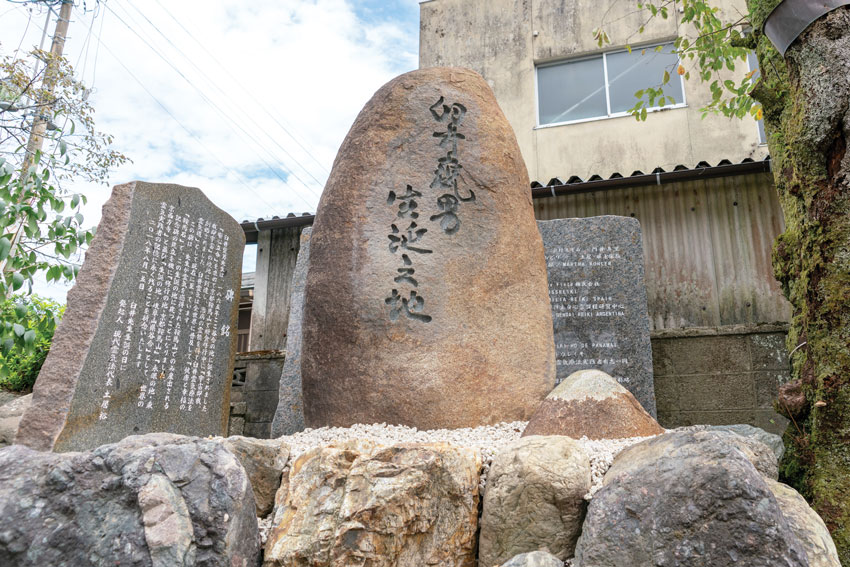 Large engraved memorial stones arranged among rocks and gravel outside a building under a partly cloudy sky.