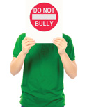 A person in a green shirt holding up a white sign with a red "Do Not Bully" circle and bar symbol.