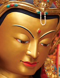 Medicine Buddha Close-up of a golden Buddha statue face with colorful jewels and serene expression.