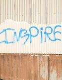 The word "INSPIRE" spray-painted in blue on a weathered, corrugated metal wall.