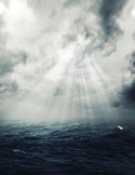Dramatic sunbeams breaking through dark, heavy storm clouds over a choppy, dark blue ocean.