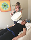 A practitioner holds a large white frame drum over a woman lying down during a sound healing session.