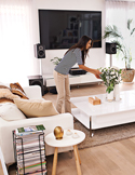 A woman arranges flowers in a bright, modern living room with clean white furniture and minimalist decor.