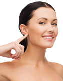 A smiling woman points toward her ear against a white background, representing hearing or ear health.