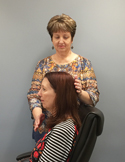 A woman stands behind a seated person, gently placing her hands on their head in a therapeutic or healing gesture.