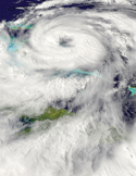 Satellite view of a hurricane showing a large, swirling white cloud formation over the ocean and islands.