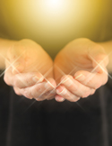 Close-up of open hands glowing with bright, sparkling spiritual light against a dark background.