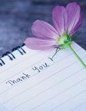 A purple flower rests on a spiral notebook page where the words "Thank You!" are handwritten in blue ink.