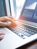 Close-up of hands typing on a laptop keyboard with a financial growth chart displayed on the screen.