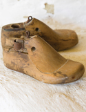 Two antique wooden shoe lasts used for shaping footwear, showing worn textures and metal loops.