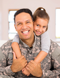 A smiling man in a military camouflage uniform giving his young daughter a piggyback ride.
