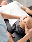 A physical therapist using both hands to stabilize and treat a patient's knee on a massage table.