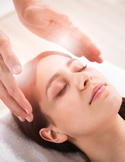 Close-up of a woman with eyes closed receiving a Reiki energy healing treatment on her head.