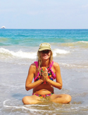 A woman sitting in a meditative prayer pose in the shallow surf of an ocean beach.