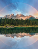 A vibrant circular rainbow over a mountain range reflected in a still, clear lake.
