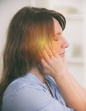A woman with closed eyes performs a self-Reiki hand position on her head with a soft yellow glow.