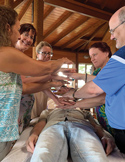 A group of people circle a man lying on a table, holding their hands over him in a Reiki healing session.