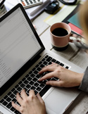 Close-up of hands typing on a laptop keyboard next to a pink coffee mug and a calculator.