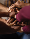 Multiple hands of various skin tones are stacked on top of one another in a symbol of unity and cooperation.