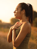 A woman stands in a golden field at sunset, eyes closed, with her hands crossed over her heart.