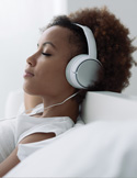 A woman rests her head back with her eyes closed, wearing large white over-ear headphones.