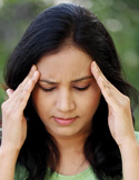 A woman closing her eyes and pressing her fingers to her temples to soothe a headache.