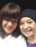 A close-up, smiling portrait of two women, one wearing a black knit beanie, leaning their heads together.