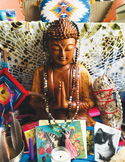Wooden Buddha statue on a spiritual altar with malas, feathers, a candle, and a photo of a cat.