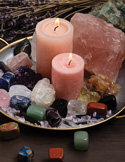 A tray holding two pink pillar candles surrounded by various colorful healing crystals and dried lavender.