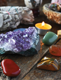 A lit candle surrounded by colorful crystals and gemstones on a wooden surface, creating a calm, spiritual atmosphere.