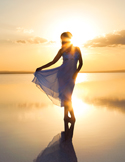 Person standing barefoot in shallow water at sunset, holding a flowing dress as golden light reflects on the surface.