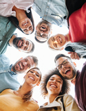 Diverse group of people standing in a circle, smiling and looking down toward the camera in a moment of connection.