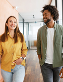 A man and woman smiling and walking together in a bright office hallway.