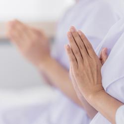 Close-up of two people in white clothing holding their hands in a prayer position, creating a calm and reverent atmosphere.
