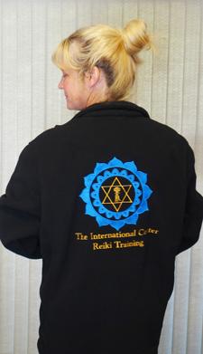 Person wearing a black fleece jacket with a large blue and gold Reiki emblem and “The International Center for Reiki Training” on the back.