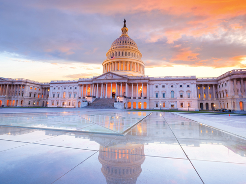 U.S. Capitol building at sunrise, its dome and columns glowing in warm light.