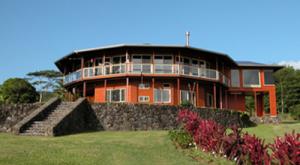 Round, two-story building with large windows and a stone base, set on a grassy. landscaped hill.