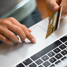 Close-up of hands using a laptop while holding a credit card, suggesting an online purchase.